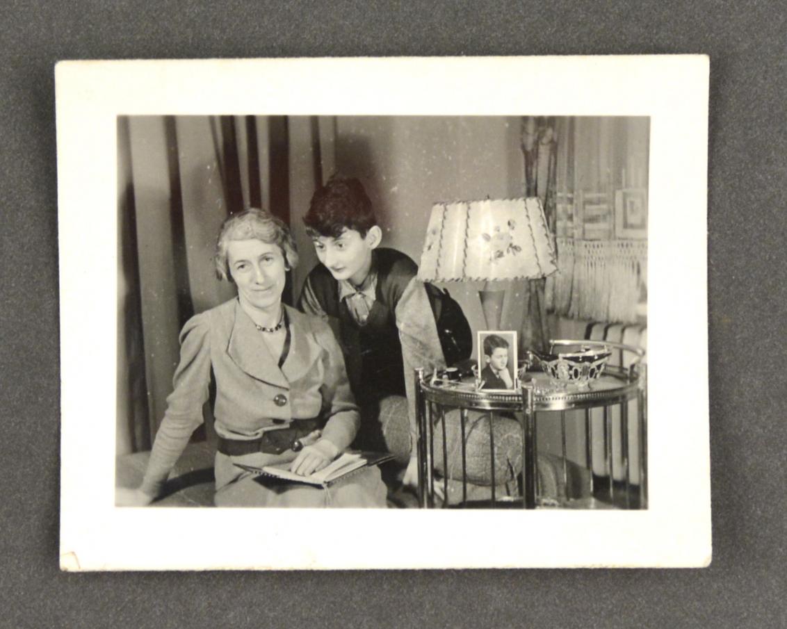 Eine Frau und ein Kind neben einem Tischchen mit Stehlampe, auf dem Tisch steht ein Fotoporträt eines Jungen