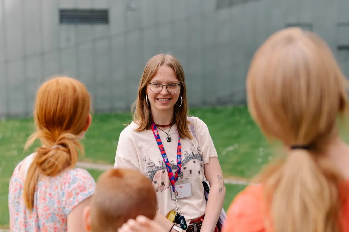 Visitors are standing with a young woman in a meadow in front of a steel building
