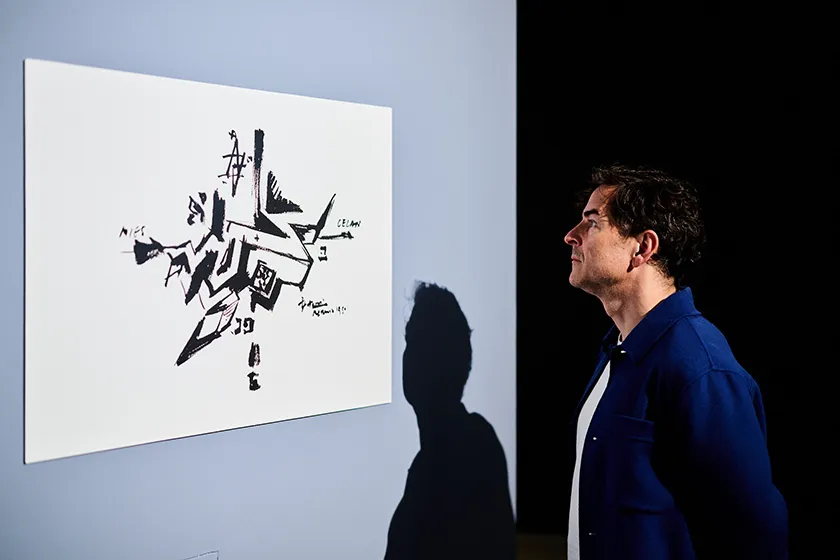 A man studies a sketch which is presented hanging at a wall.
