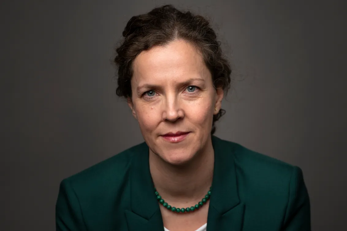 Frau schaut freundlich in die Kamera. Sie tr&auml;gt einen gr&uuml;nen Blazer.