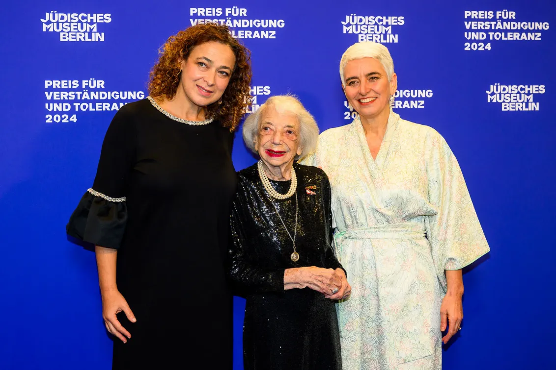 Three women are standing on a blue carpet and smile.