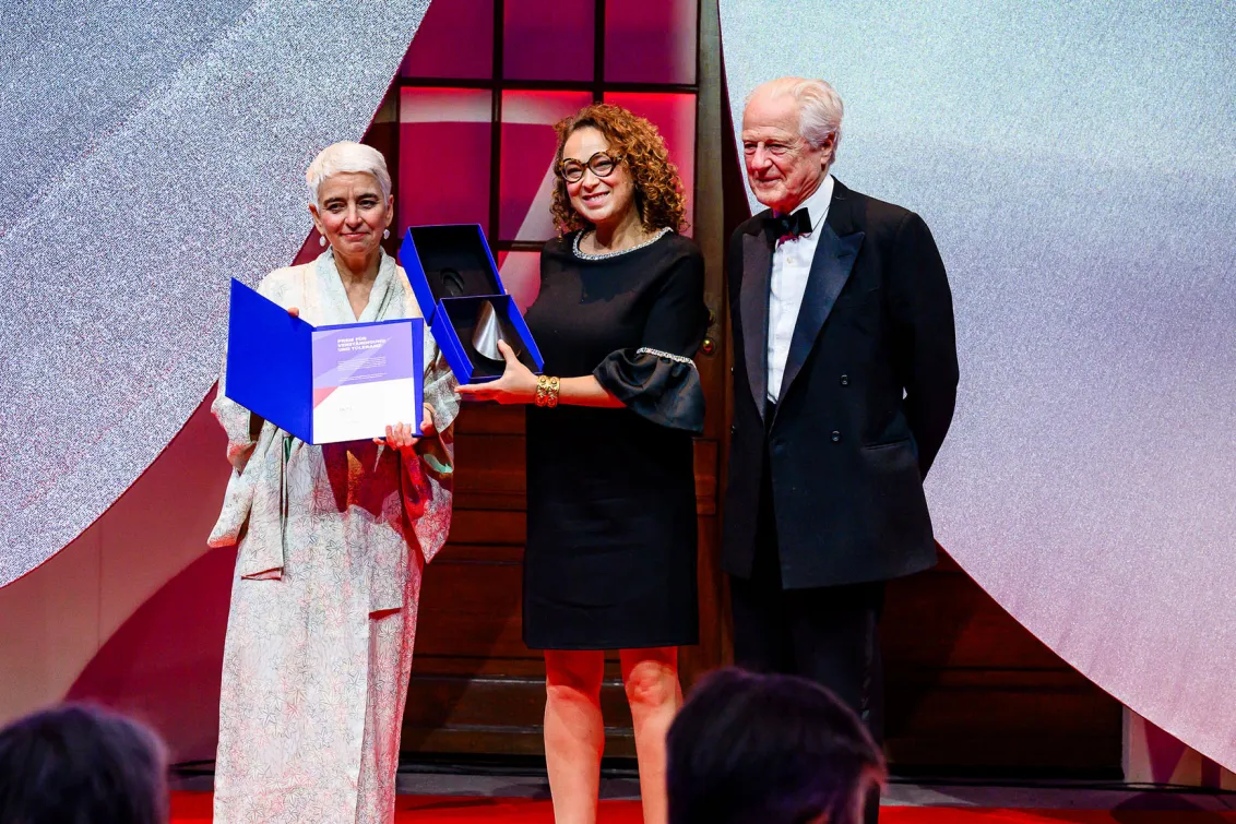 Three people are standing together and smiling, two of them holding their prizes.