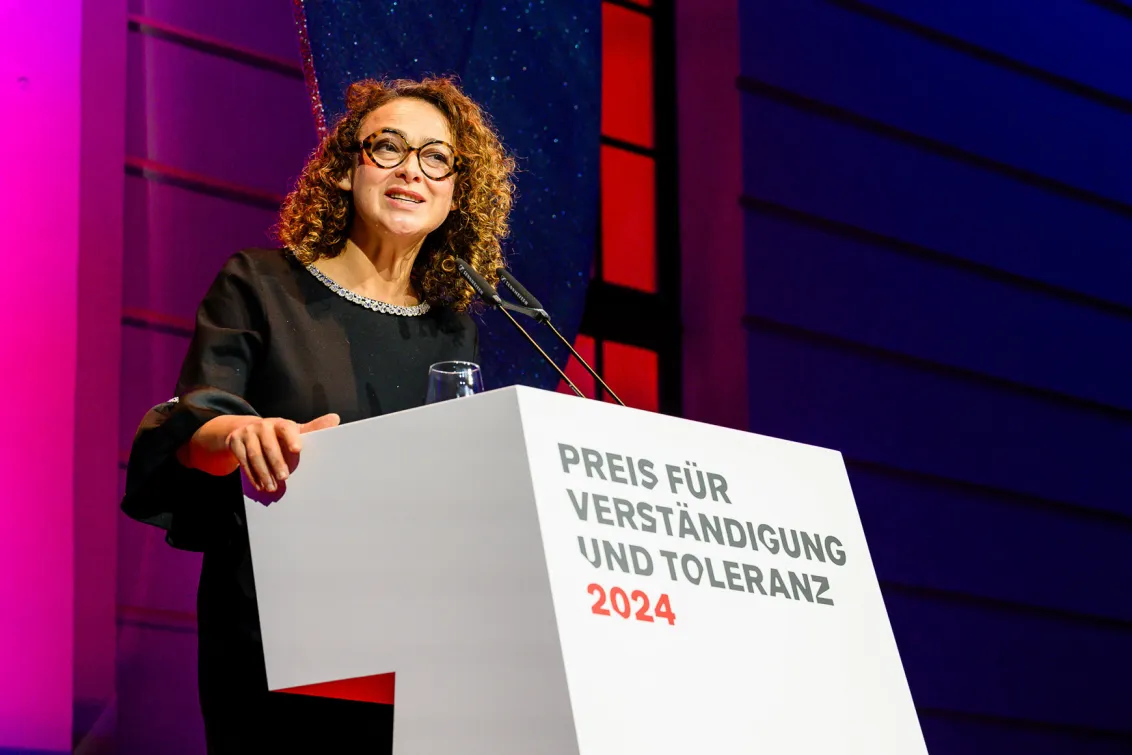 A woman stands at a podium desk and delivers a speech.