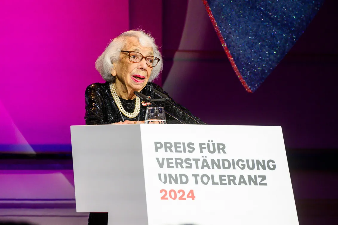 A woman stands at a podium desk and delivers a speech.