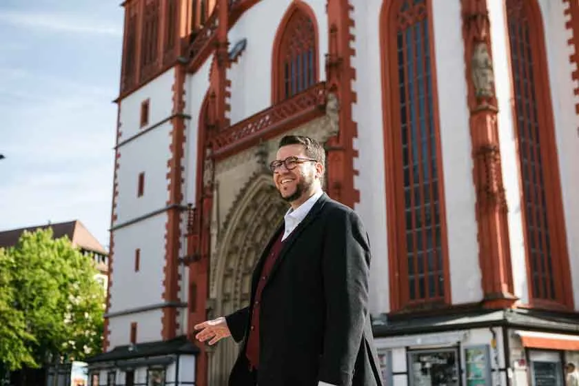 Ein Mann in einem Anzug steht vor einem Geb&auml;ude.