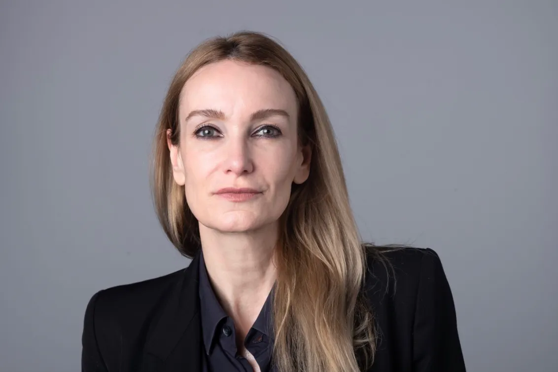 Porträt einer Frau mit langen blonden Haaren, die in die Kamera schaut.