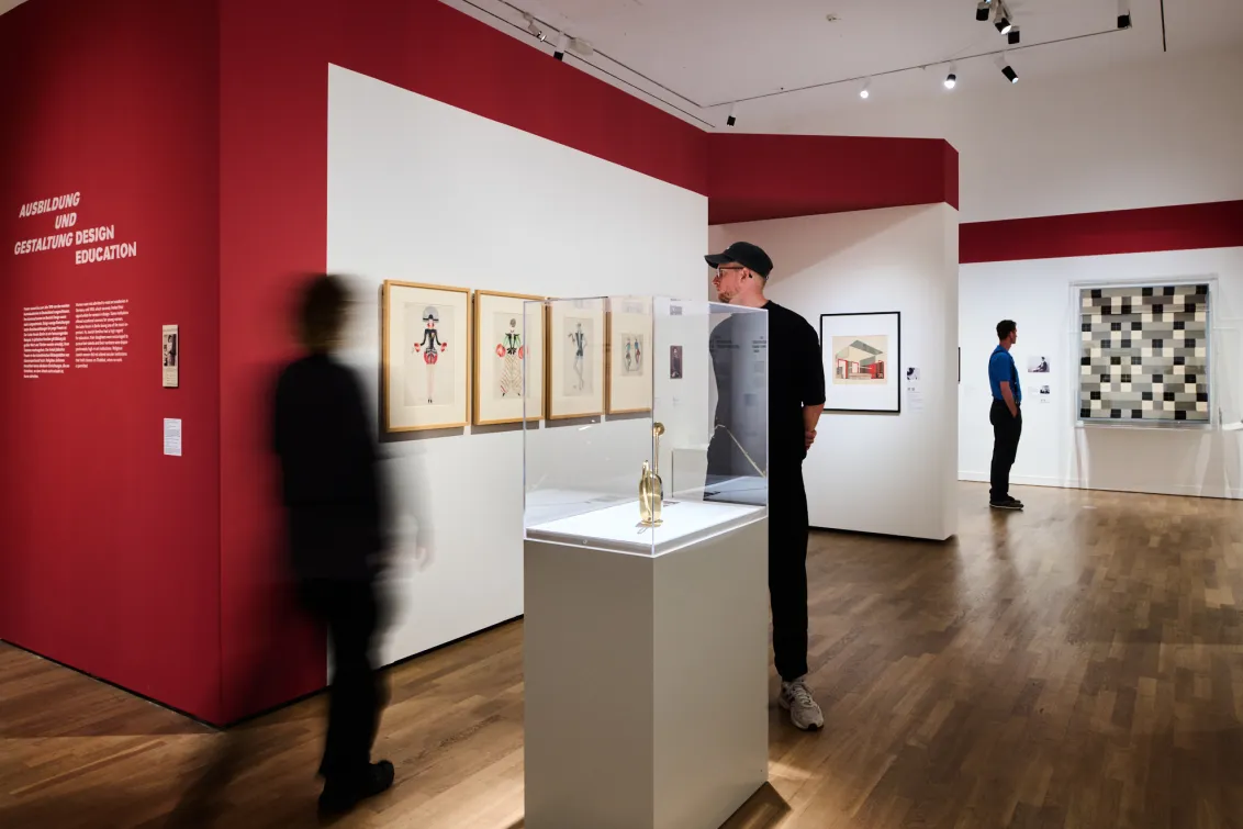 Ausstellungsansicht mit zwei Personen und Objekten, die in Vitrinen liegen oder an der Wand hängen.
