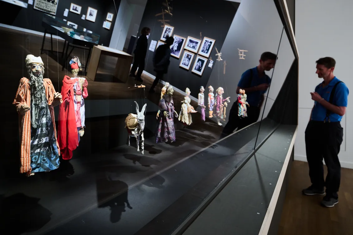 Ausstellungsansicht mit einer Person und einer Reihe von Puppen, die in einer Vitrinen präsentiert werden.
