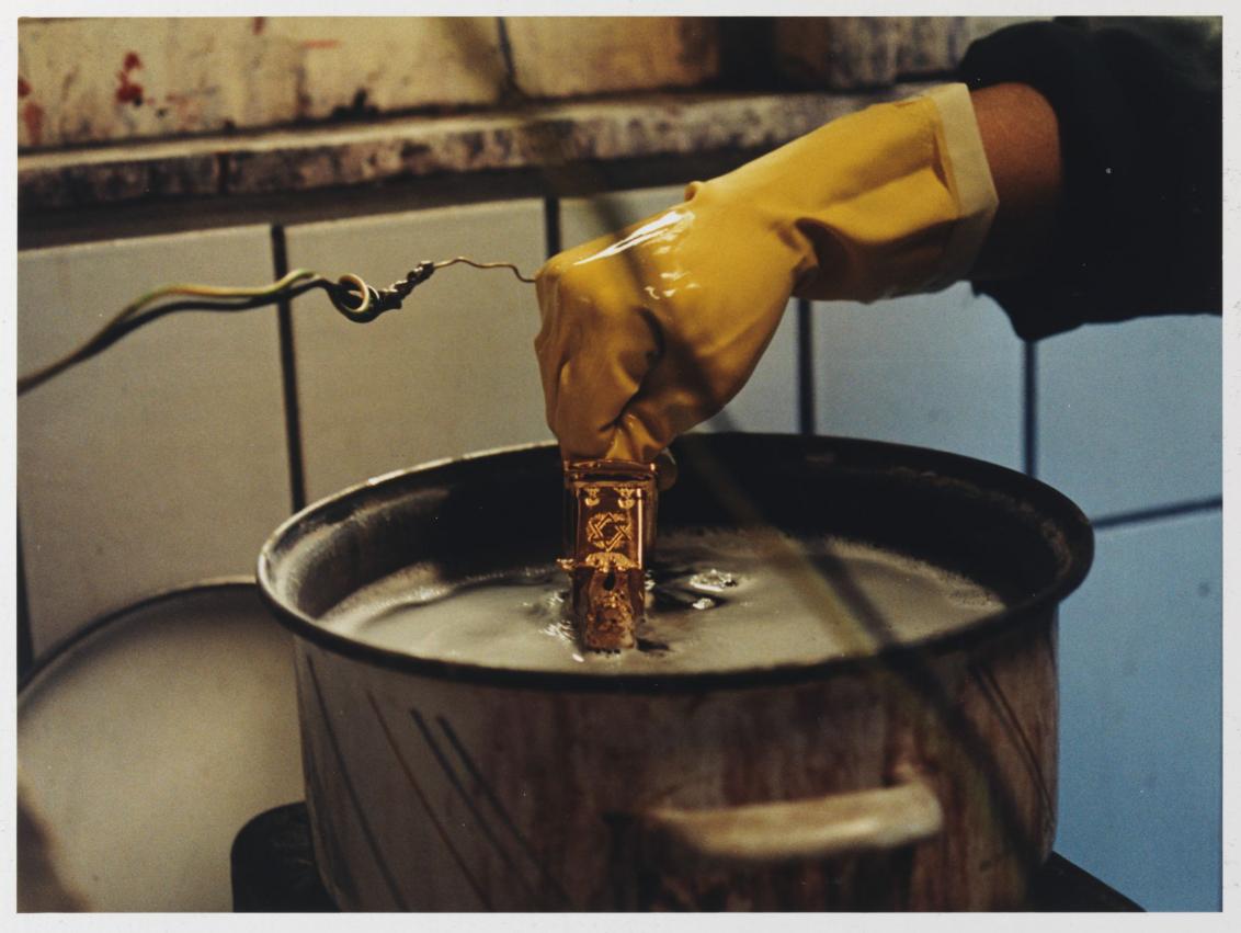 A gloved hand dips a single decoration of the Hanukkah lamp into the gilding.