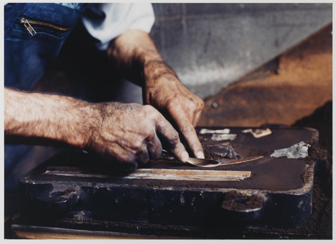 Foundryman Mr. Ehrlich makes a mold from dark sand.