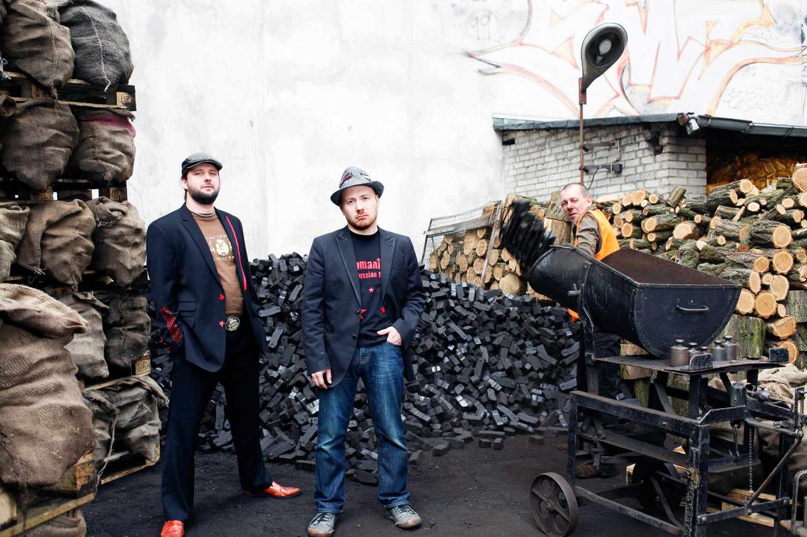 Three band members in front of a backdrop of firewood and coal