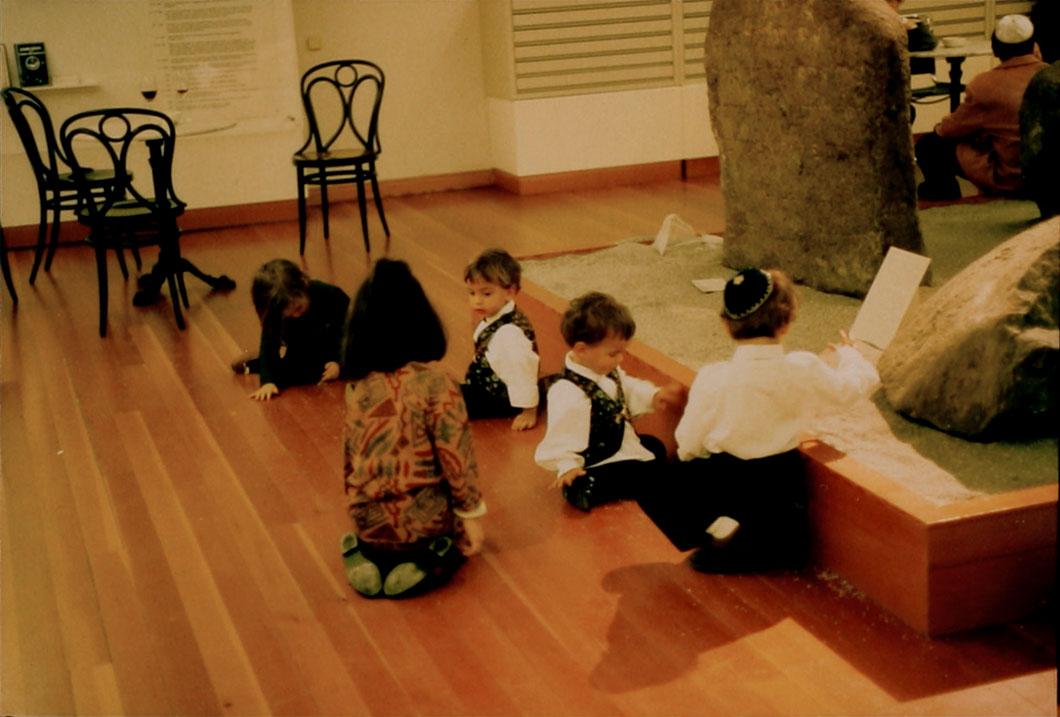 Exhibition space with five children playing next to a kind of sandbox with gravestones.