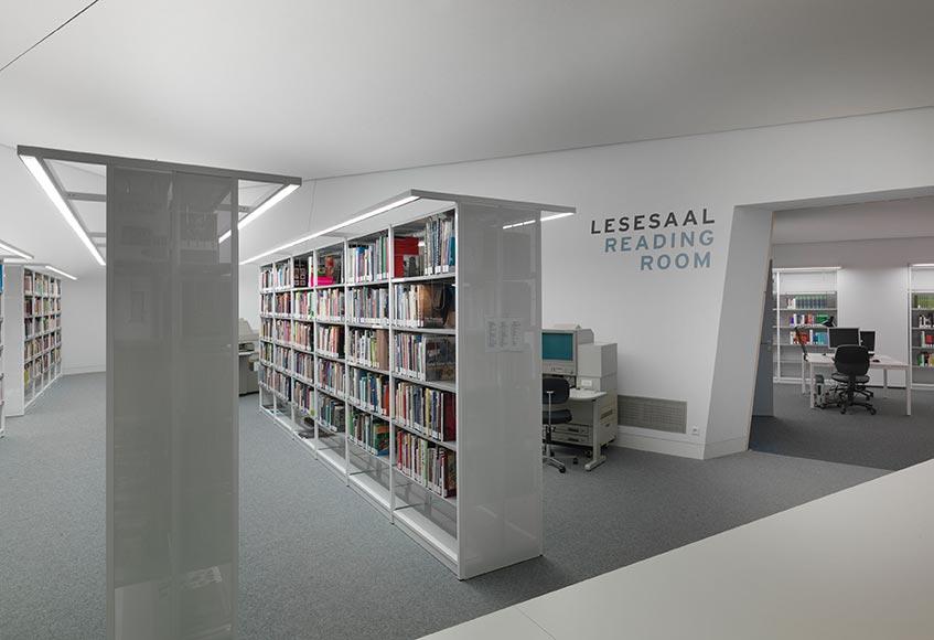 Blick auf weiße Bücherregale mit bunten Buchrücken im Lesesaal der Bibliothek des Jüdischen Museums Berlin in der W. Michael Blumenthal Akademie