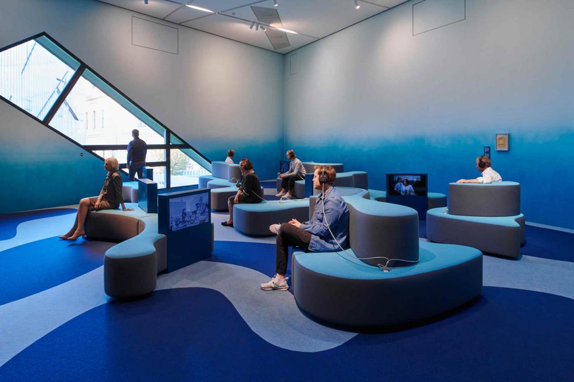 Sala en tonos azules con asientos en forma de ola y pantallas de televisión empotradas