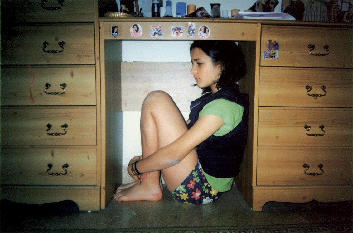 Girl in shorts crouches under a desk
