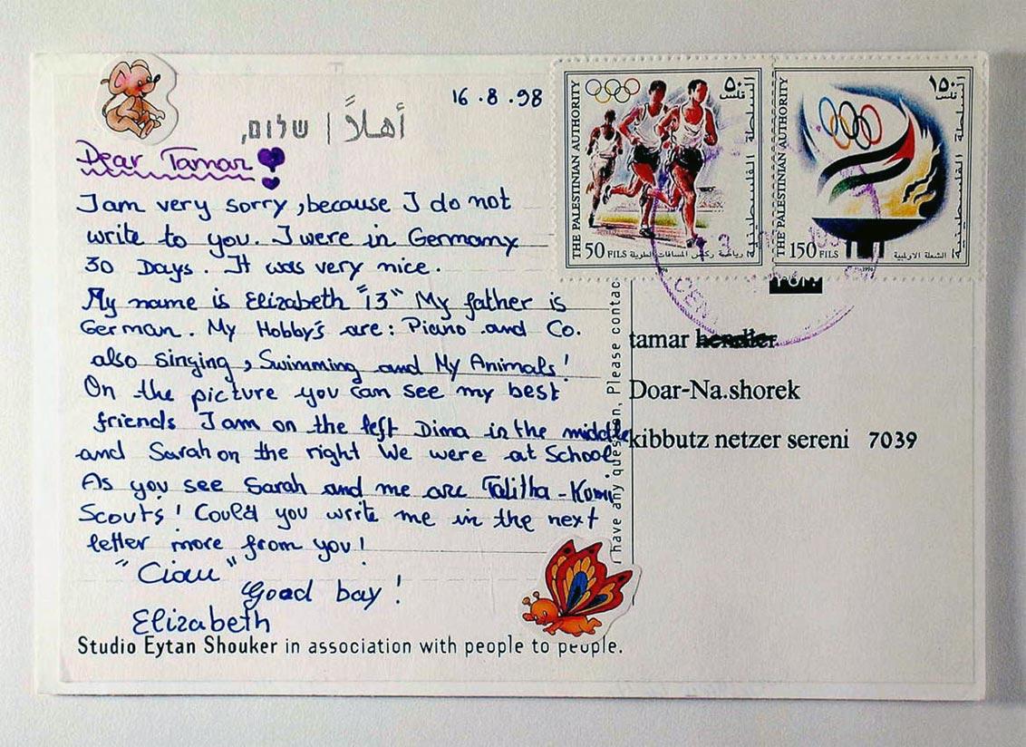 A postcard written in childlike handwriting and decorated with two stickers of cartoon characters. 
