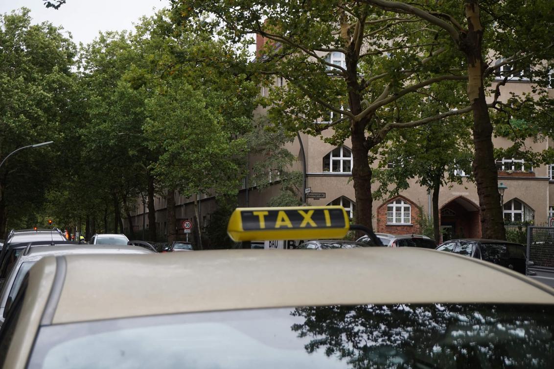 Farbfoto: Taxi in einer von Bäumen gesäumten Straße