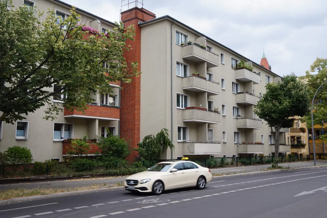 Color photo: Postwar apartment building with a taxi passing by