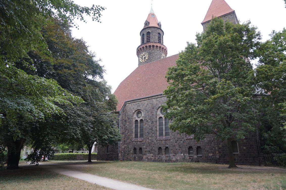 Farbfoto: Blick von einer Grünanlage zu einer neuromanischen Kirche mit zwei Türmen