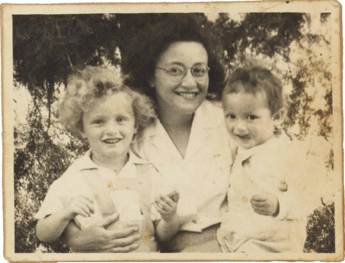 Black and white photography: Leonie is sitting in the middle and laughs. Michael, who runs his tongue over the right corner of his mouth, is sitting on her lap.On the left is Peter-Uri with bright curls, also smiling broadly.