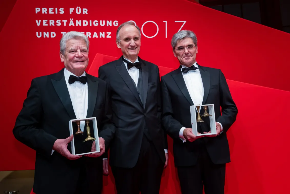 Three men in suits hold awards up to the camera.