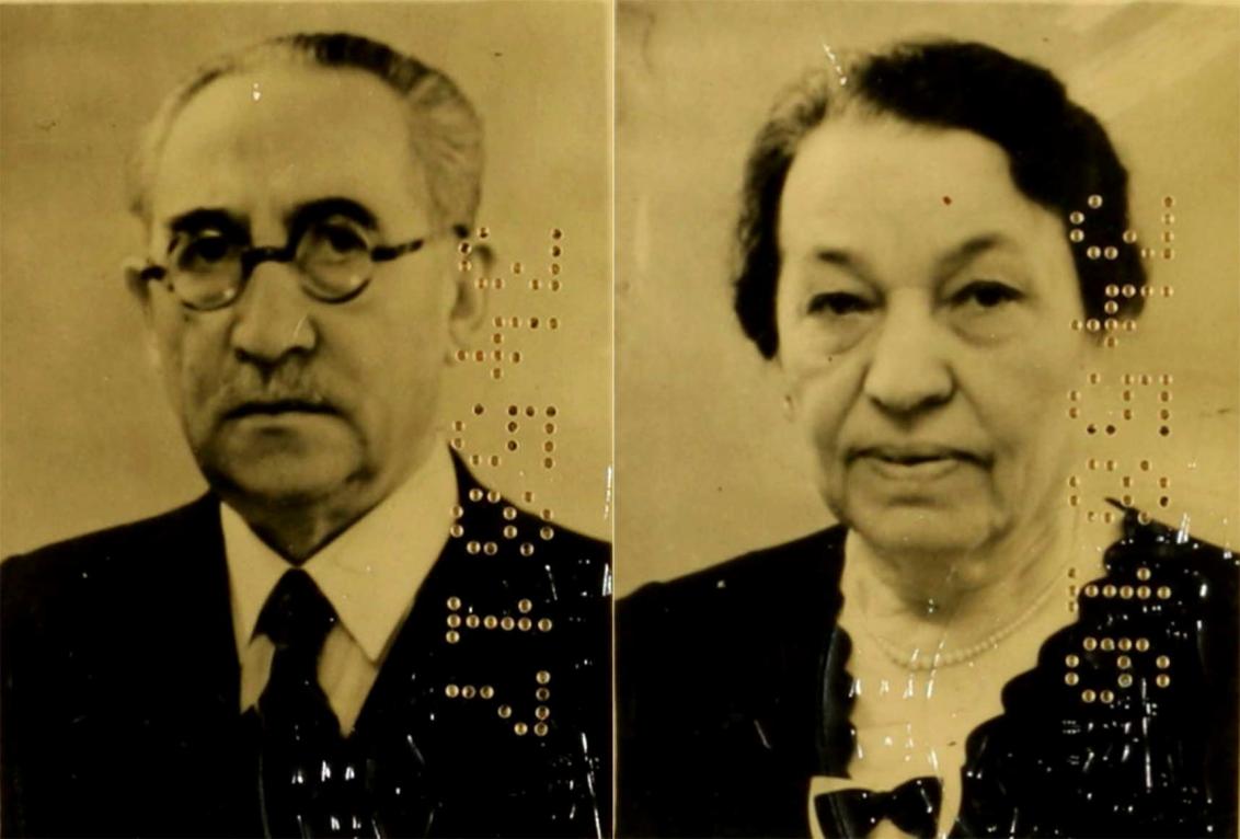Passport photo of an older man wearing glasses and a suit and necktie together with an older woman with a ribboned blouse and a necklace; the photos bear numeric codes