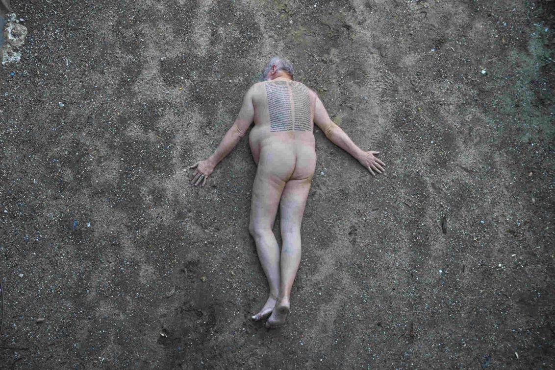 Nackter Mann mit tätowiertem Rücken liegt auf dunkler Erde