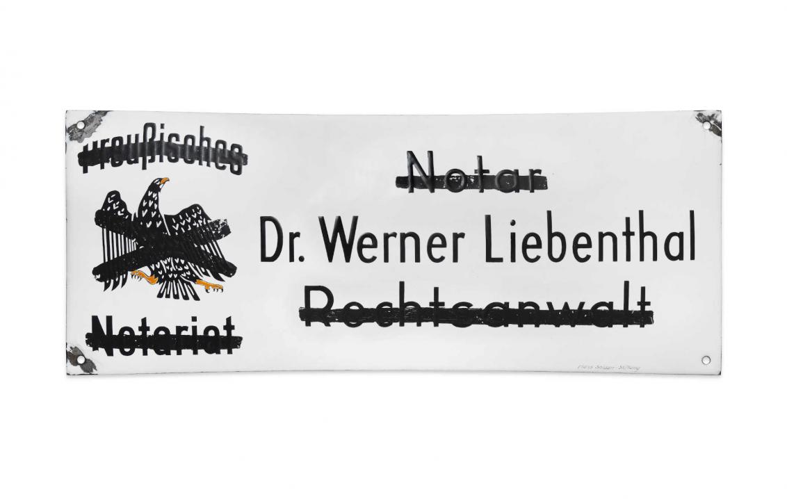Weißes Schild, auf dem Dr. Werner Liebenthal steht. Die Wörter Notar, Rechtsanwalt, preußisches Notariat und ein Adler sind durchgestrichen