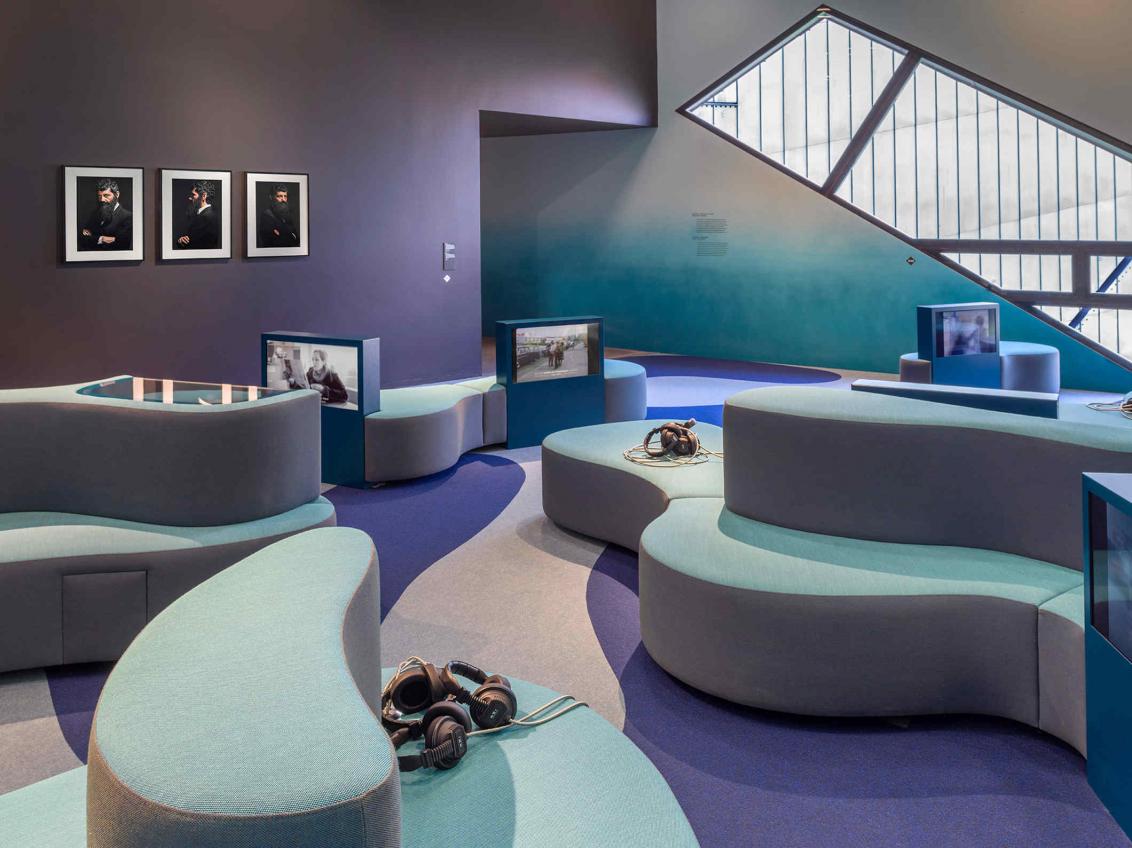 Raum mit Farbverlauf von lila zu türkisblau, Sofas, Kopfhörer, Bildschirme