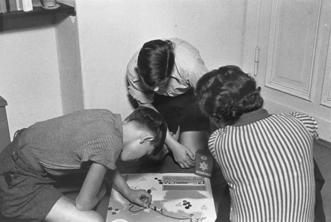 Schwarz-Weiß-Fotographie mit einer Frau und zwei Schülern, die ein Brettspiel spielen