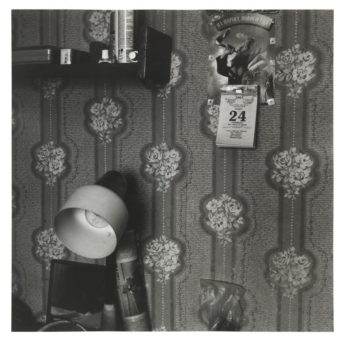 A photograph by artist Rita Ostrovska shows a wallpaper wall with calendar, in the foreground is a floor lamp.