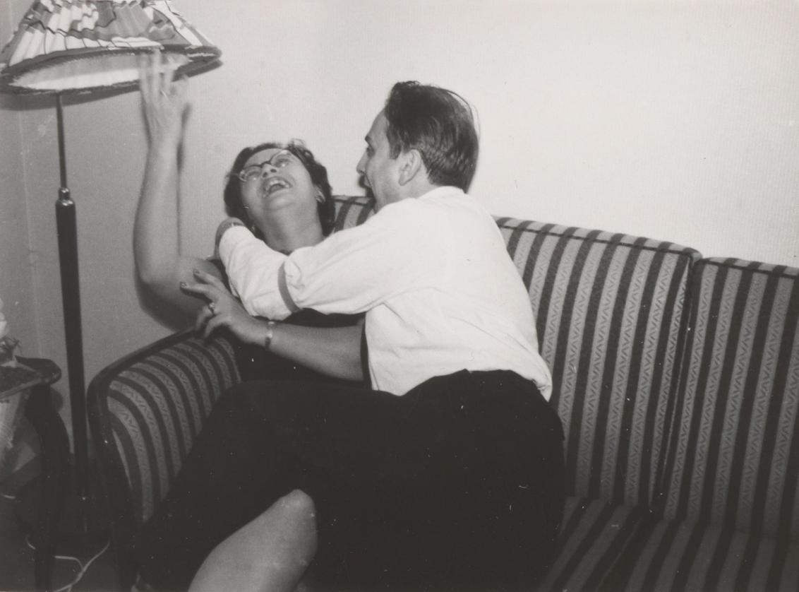 Eine Frau und ein Mann scherzen auf einem gestreiften Sofa unter einem Lampenschirm