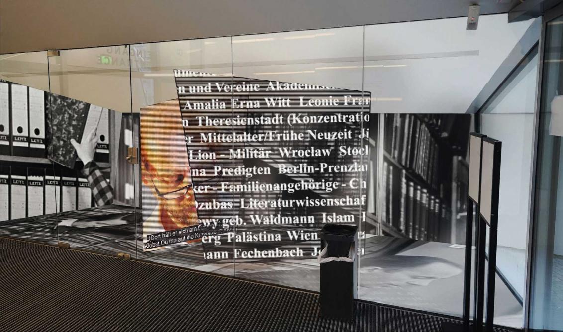 Display case with oversized photos of people, archive boxes and texts. 