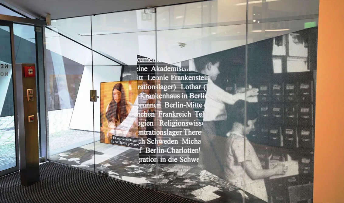 Display case with oversized photos of people, archive boxes and texts. 
