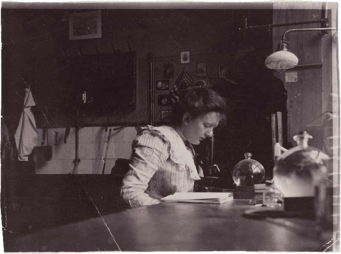 Historische Schwarz-Weiß-Fotografie  einer jungen Frau die über einen Tisch gebeugt liest.