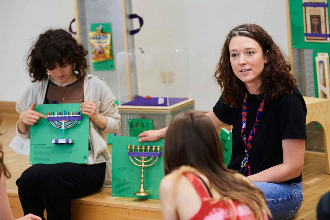 Two woman hold green squares to which Hanukkah Menorahs are attached.