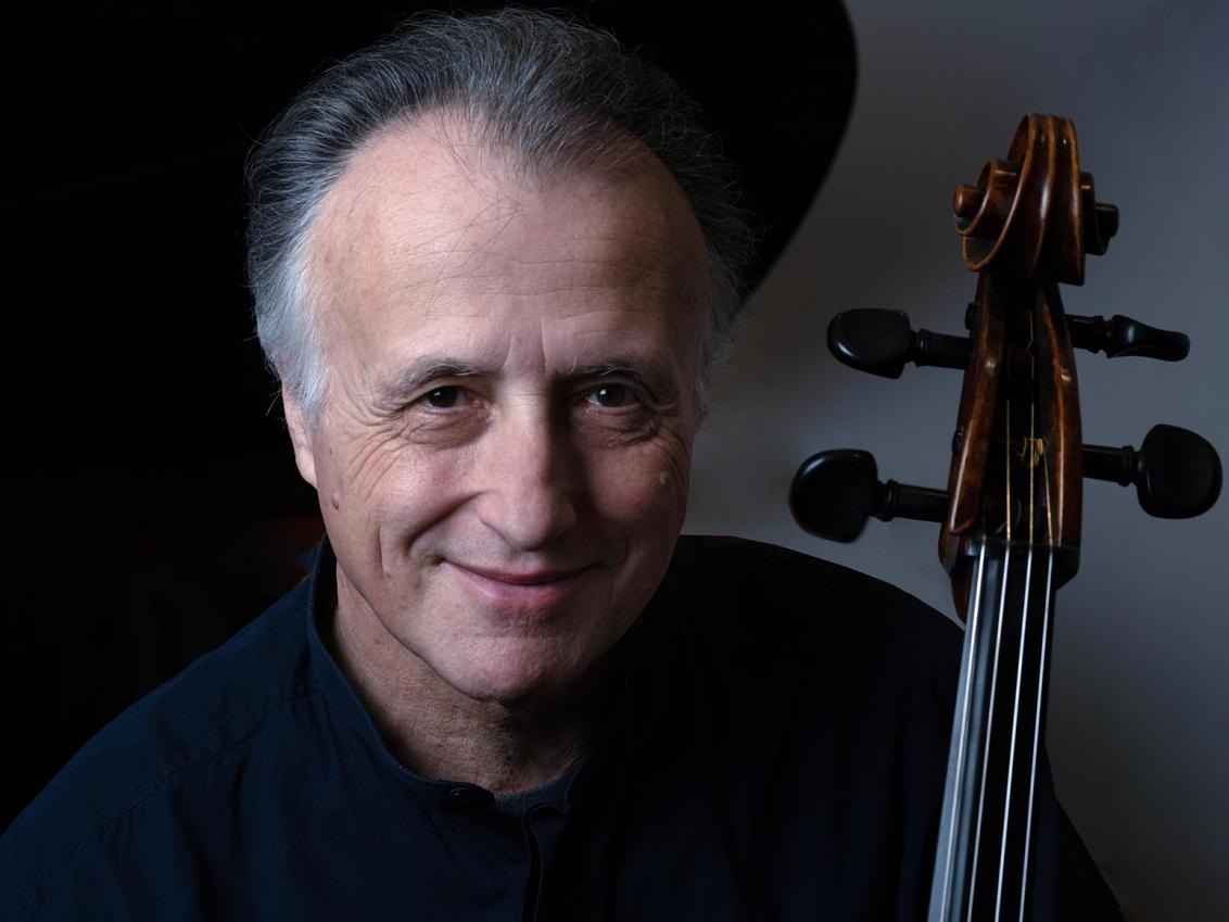 Porträtfoto eines lachenden grauhaarigen Mannes, neben seinem Kopf sind Griffbrett und Wirbelkasten eines Cellos zu sehen.