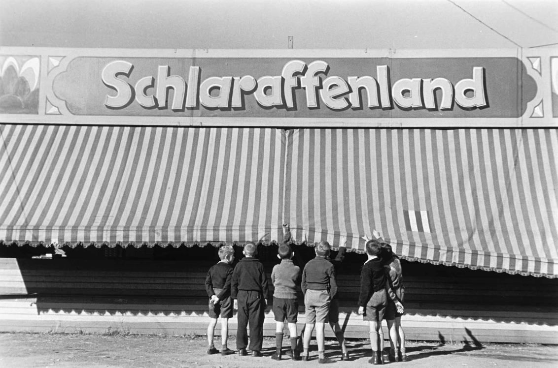 Historical photograph of a group of boys standing in front of a large tent called “Schlaraffenland” (en: Cockayne), black and white photo, ca. 1935