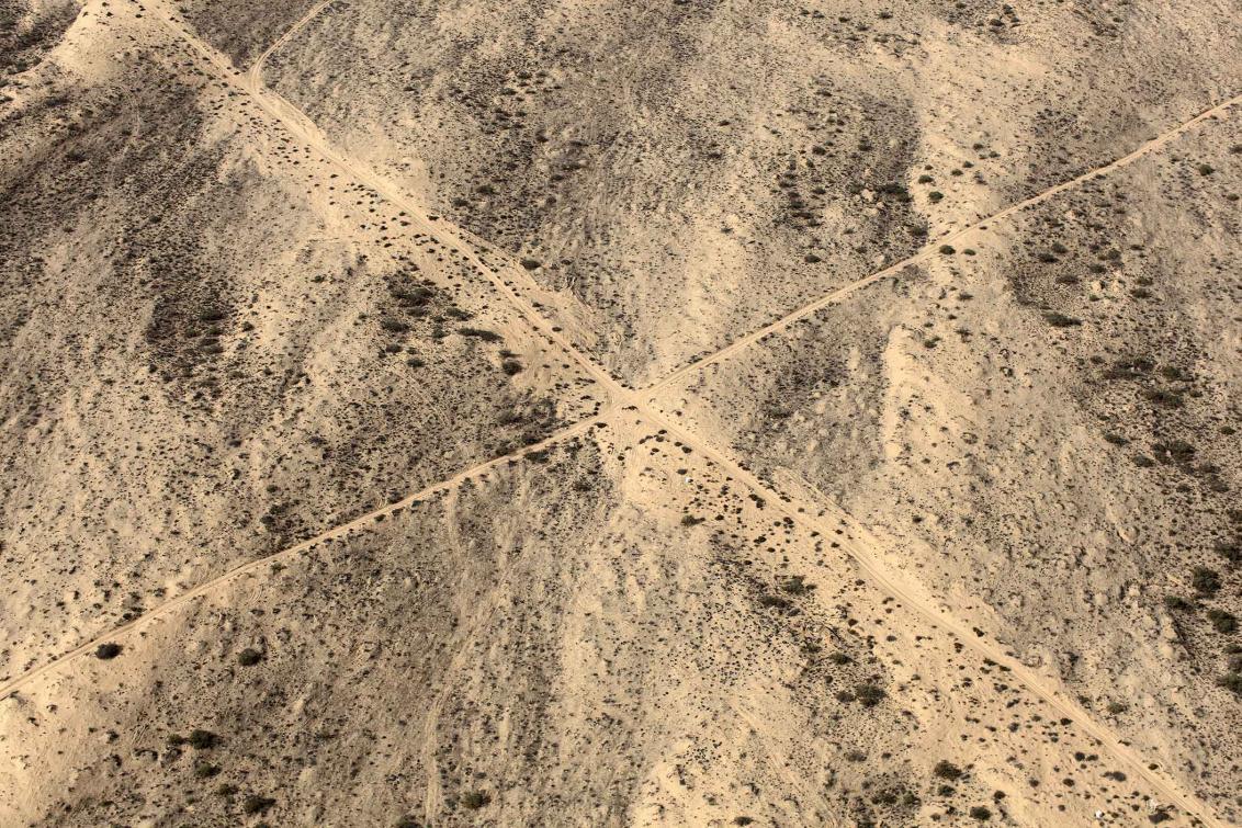 Blick von oben auf eine Wüstenlandschaft mit zwei sich kreuzenden sandigen Linien