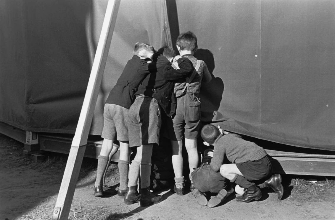 Vier Jungs sehen auf dem Jahrmarkt heimlich in ein Zelt hinein, Schwarz-Weiß-Foto