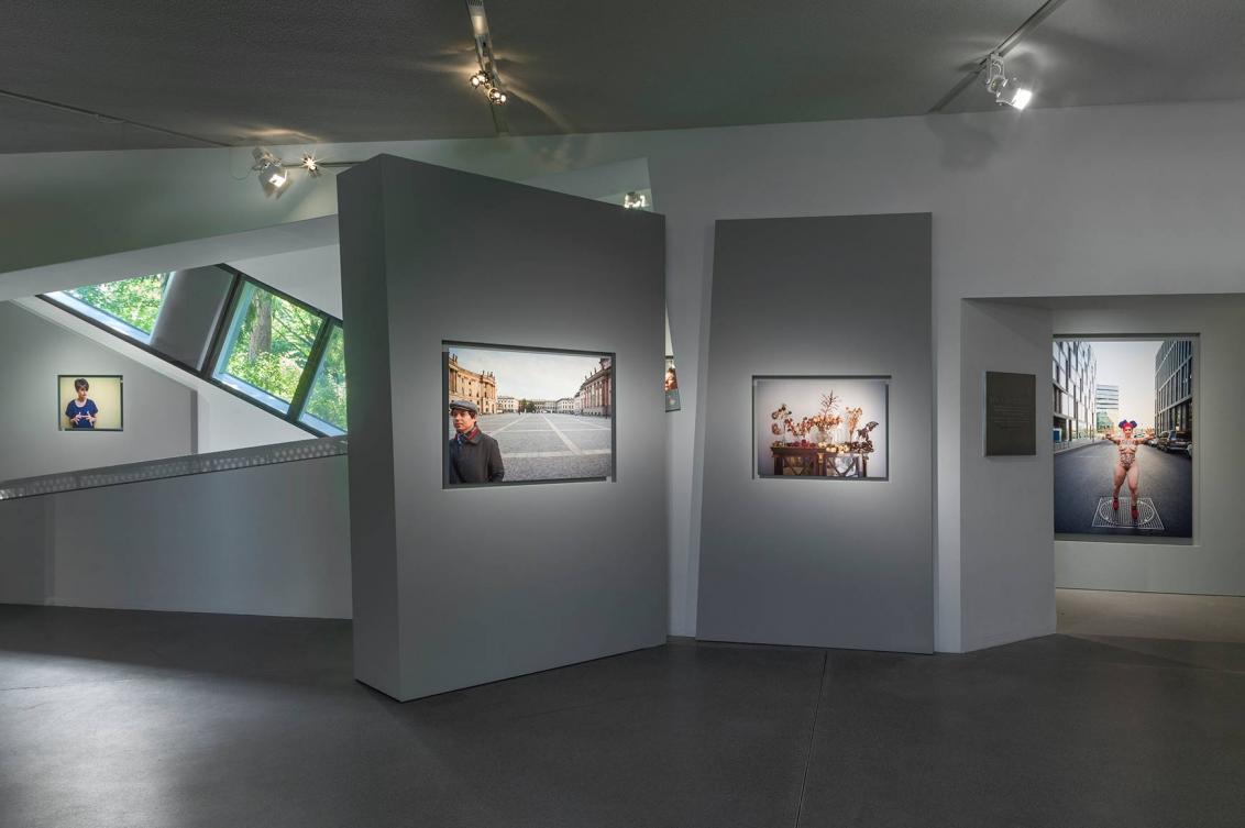 Panorama-Ansicht der Ausstellung mit vier Porträts und einem charakteristischen Fenster des Libeskind-Baus