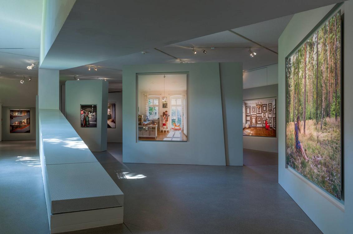 View of the exhibition with winding light gray walls, in which the colorful portrait photos are embedded