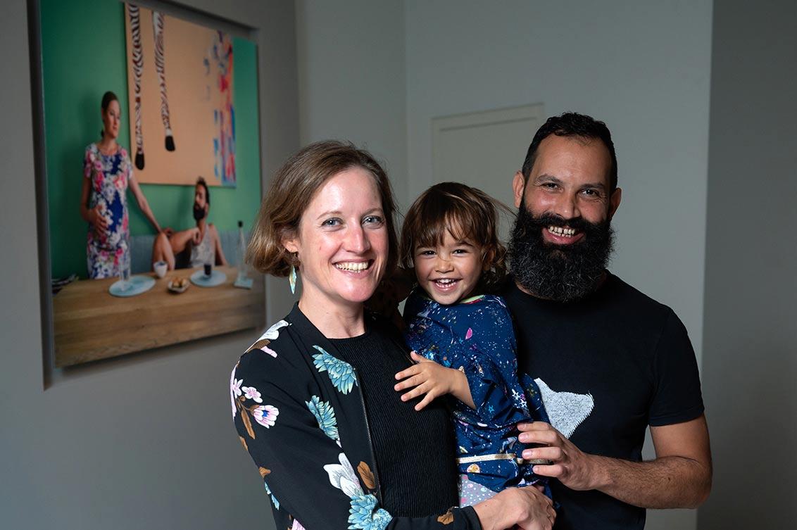 Laughing family of three in front of portrait of couple with pregnant woman