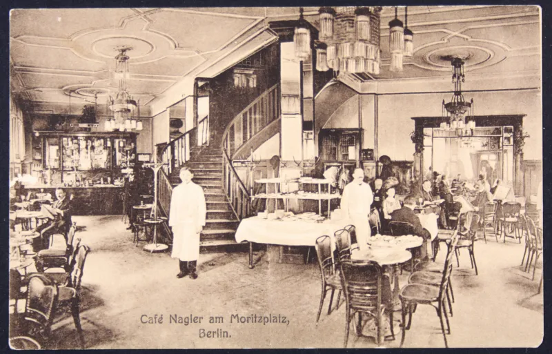 Schwarz-Weiß Bild. Innenraum eines feinen Cafés mit Tischen und Stühlen und Kronleuchtern. Im Raum befinden sich Kellner und Gäste des Cafés.