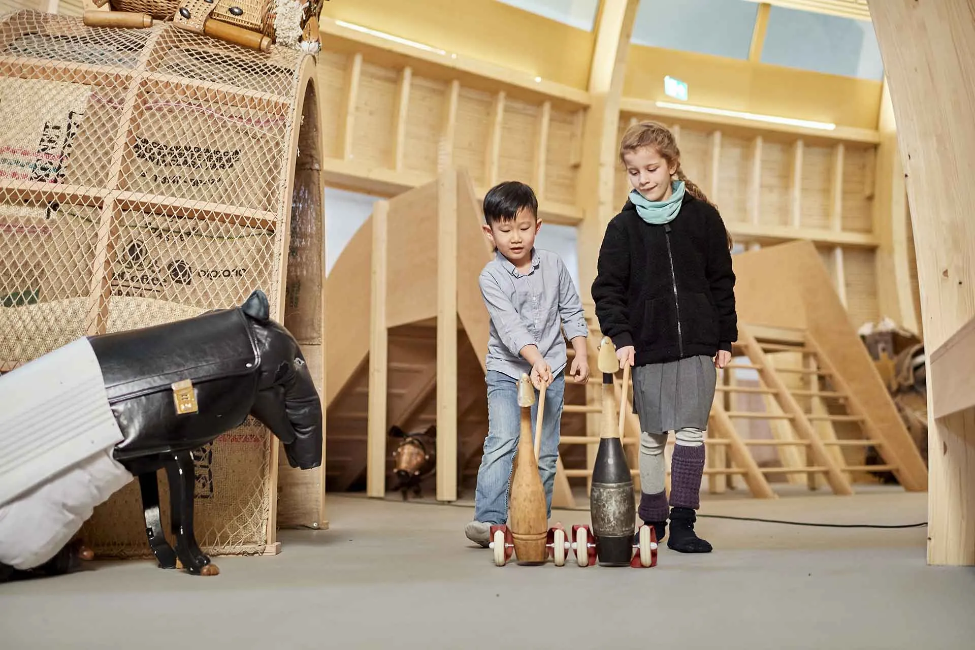 Zwei Kinder schieben jeweils eine Spielente am Stab durch das Kindermuseum ANOHA. Ein Tapirskulptur links im Bild scheint ihnen zuzuschauen.
