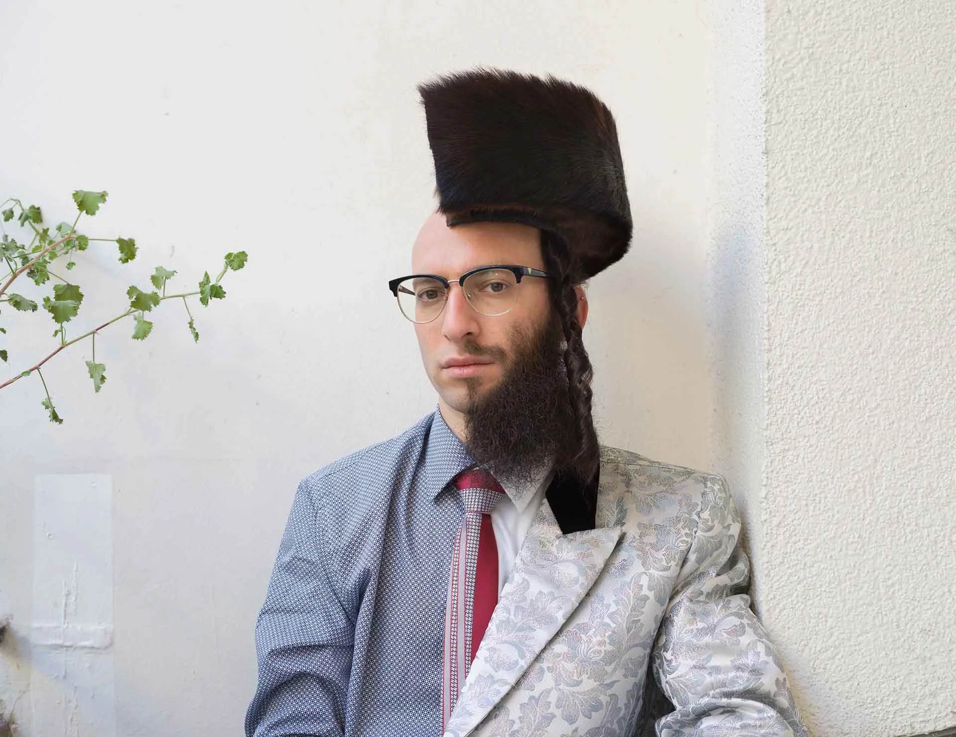 Photograph of a man divided along the longitudinal axis, as it were, into two halves: on the left side he wears a shirt and bald head, on the right a full beard and a (halved) shtreimel on his head