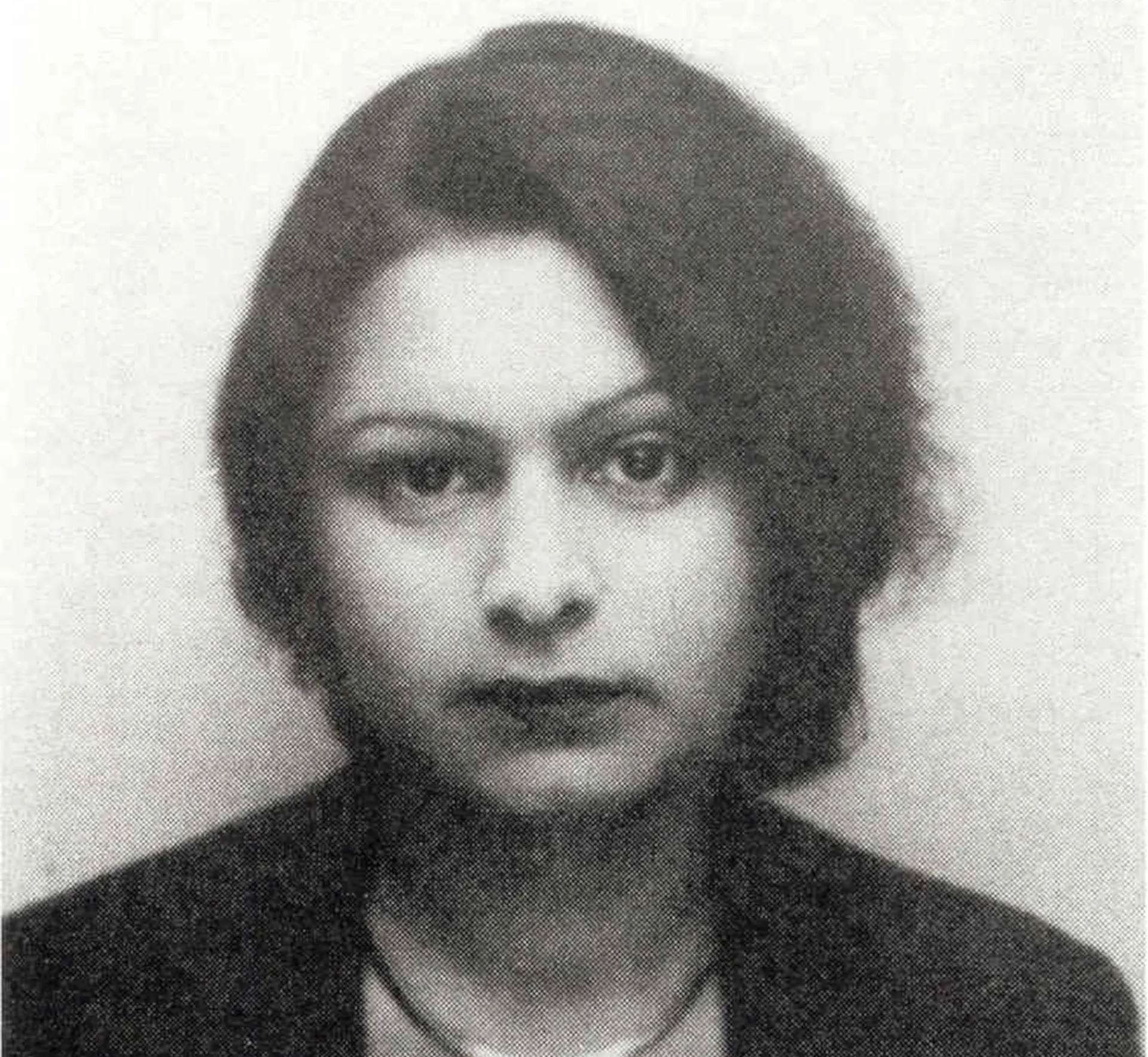 A woman with dark hair looks into the camera. It is a black-and-white photograph.