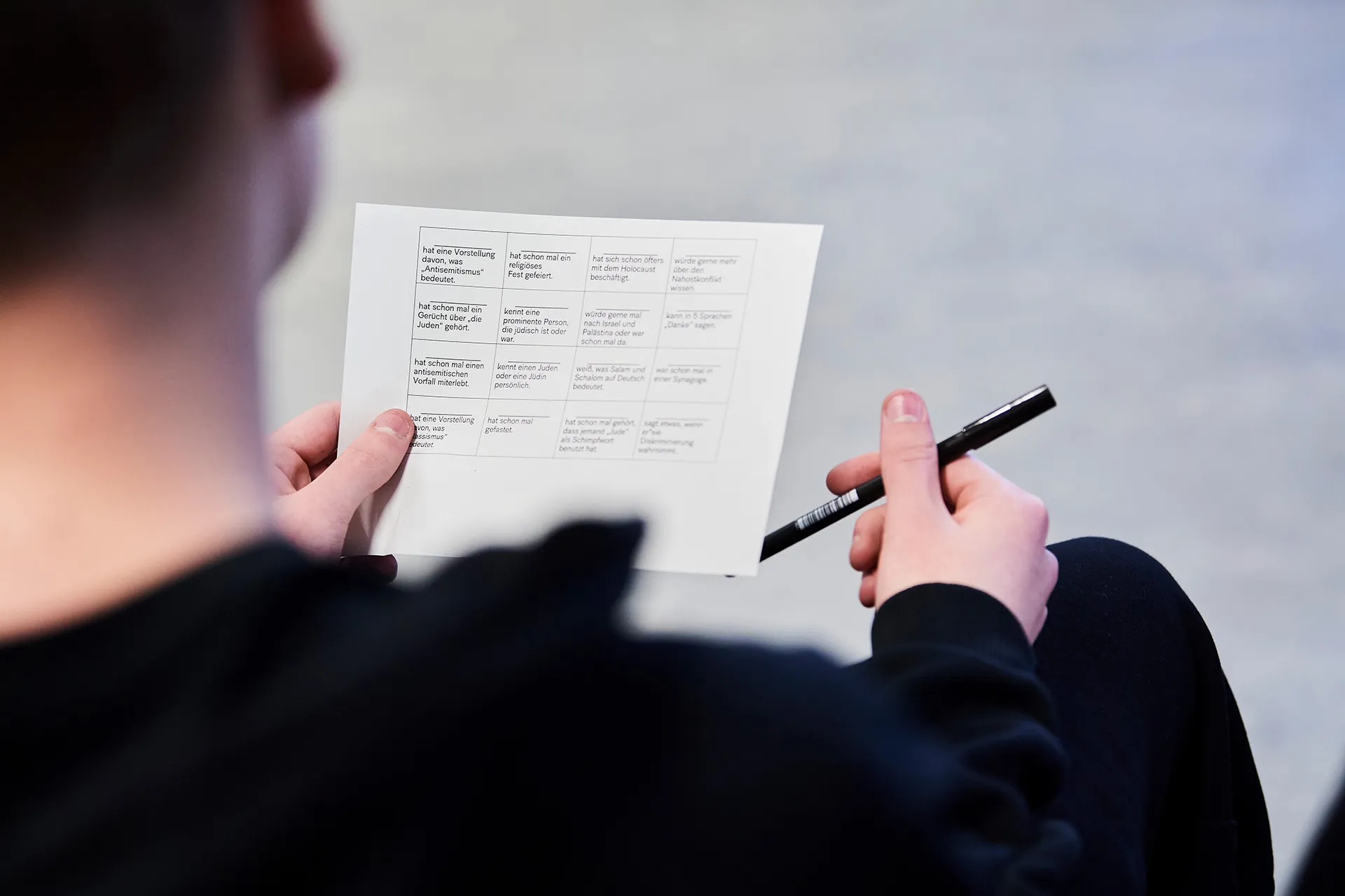 View over the shoulder of a person holding a worksheet in their left hand and a pen in the other.