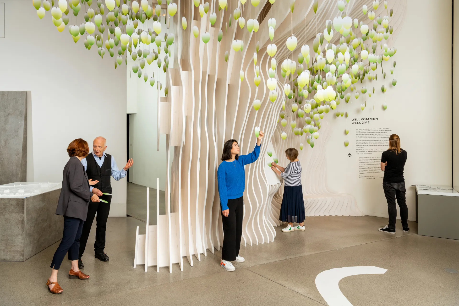 Mehrere Menschen stehen an einem Baum aus Holz. Sie sind in einem Museum