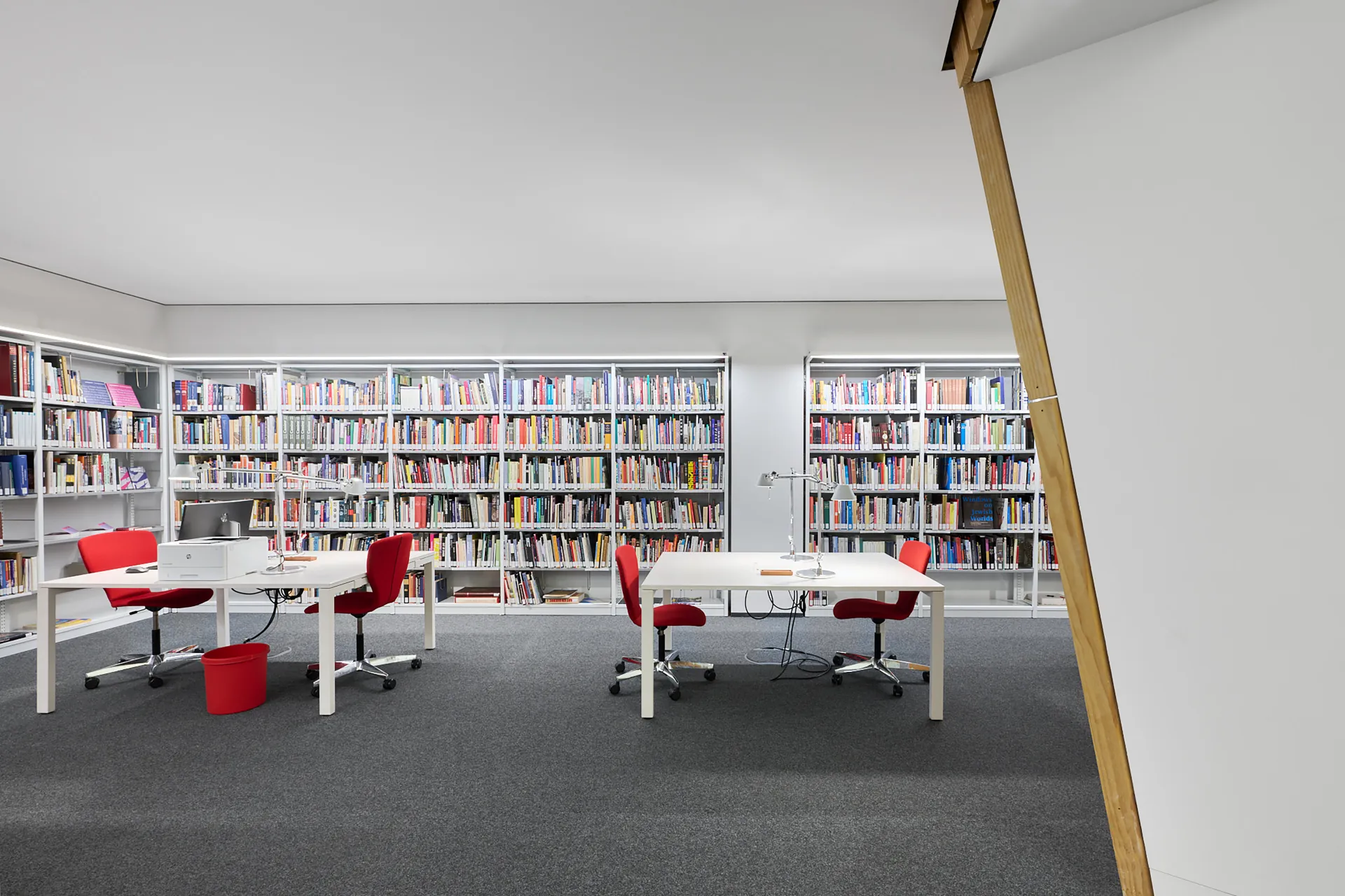 Das Bild zeigt Regale mit Büchern und zwei Schreibtische mit jeweils zwei Stühlen.